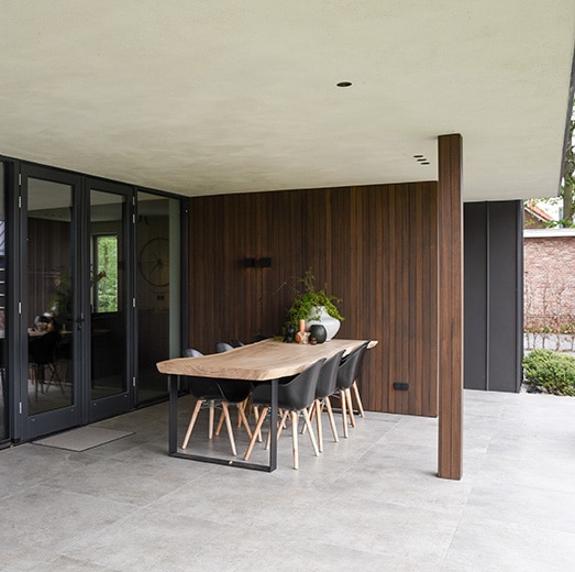 Overdekt terras met buitentafel en stoelen op een lichtgrijze natuursteen look vloer