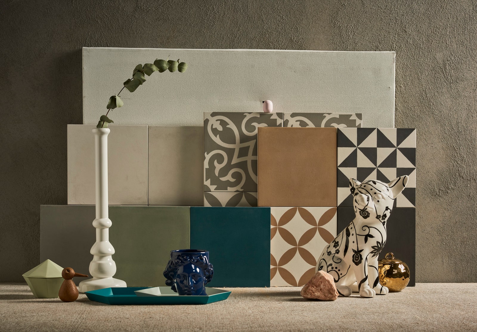 Collectie van tegels met Portugese patronen in neutrale kleuren, gestyled met moderne decorstukken zoals een witte kandelaar, blauwe vaas en decoratief beeldje.