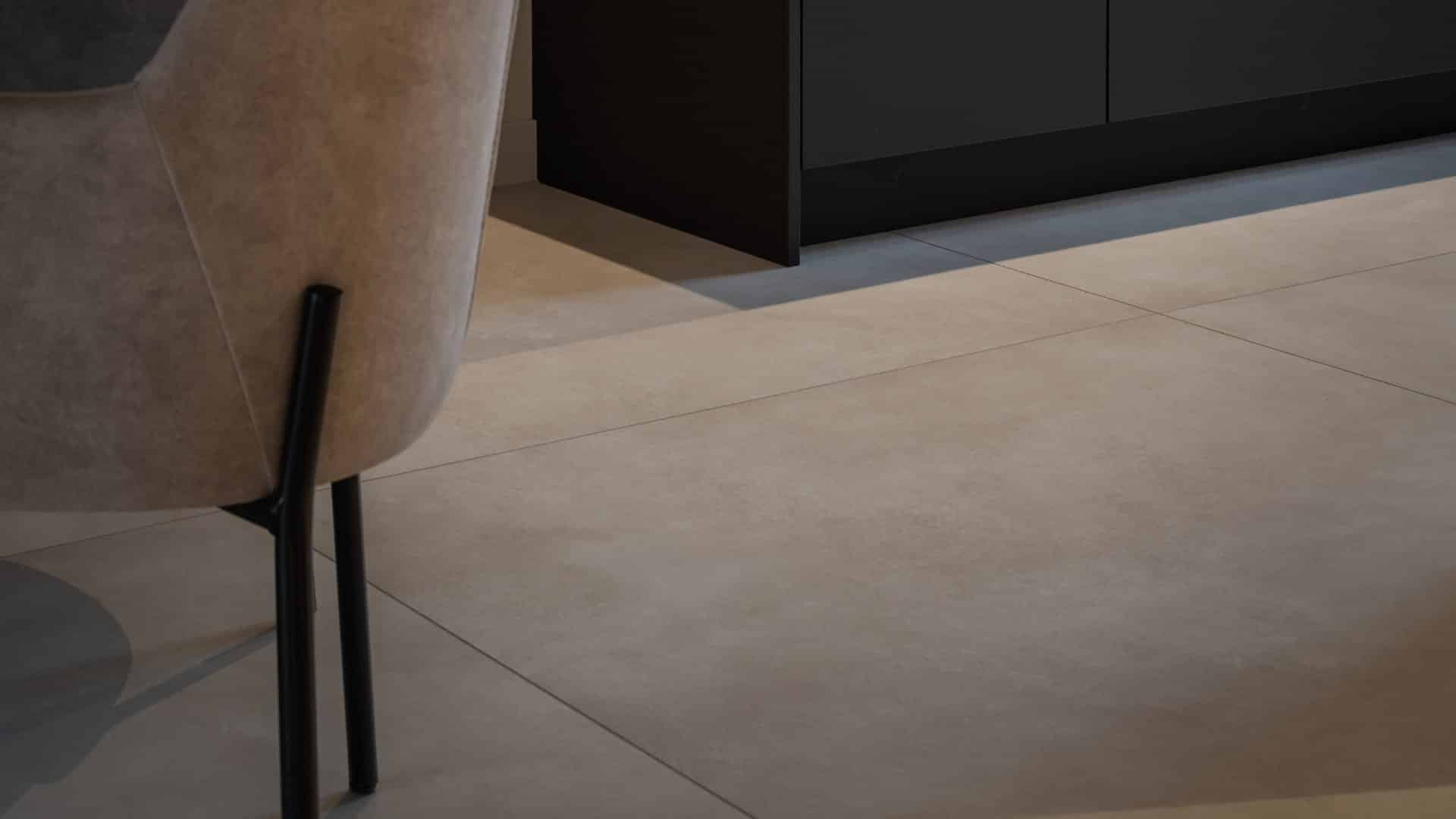 Close-up van een living met woonkamer tegels in betonlook. Een beige stoel biedt een subtiel kleuraccent, terwijl een zwarte kast voor groot contrast zorgt.